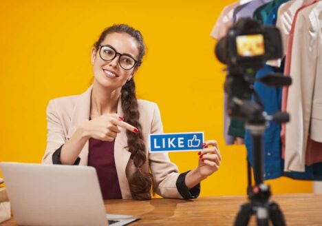 Female on laptop holding Facebook like sign