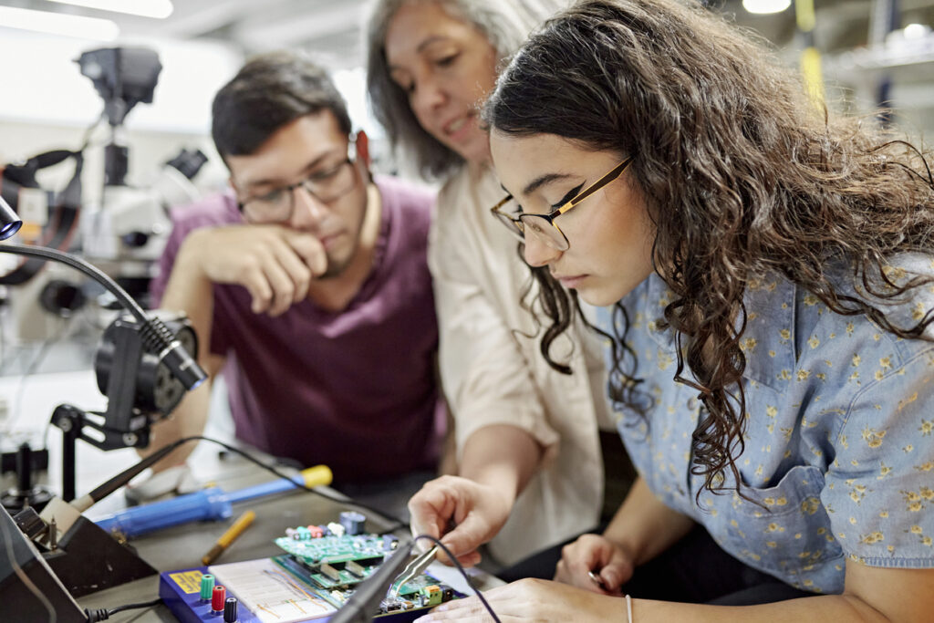 Female professor supporting male and female university students with an electrical BEng engineering degree project