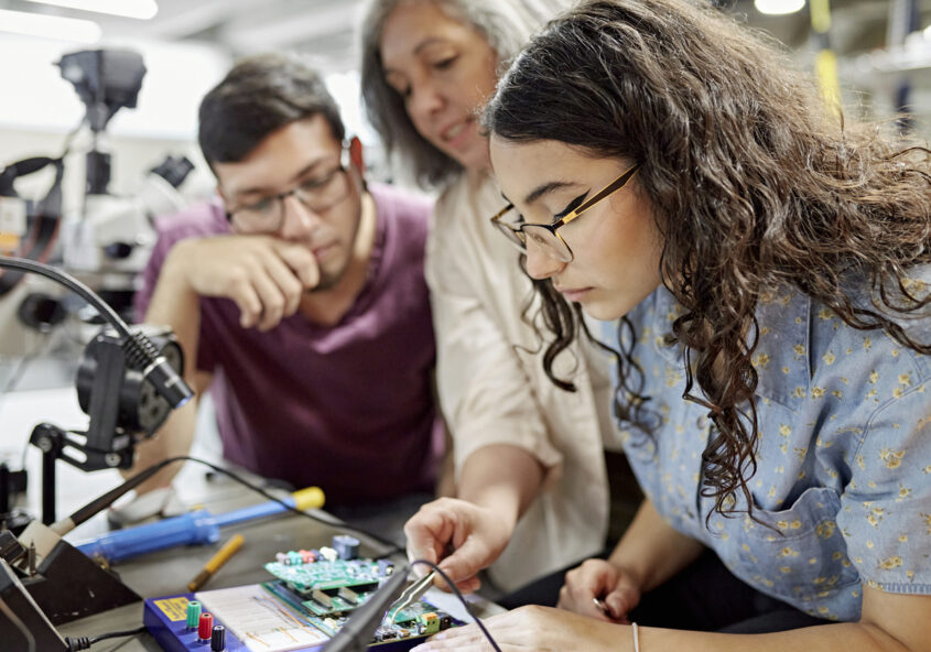 Female professor supporting male and female university students with an electrical BEng engineering degree project